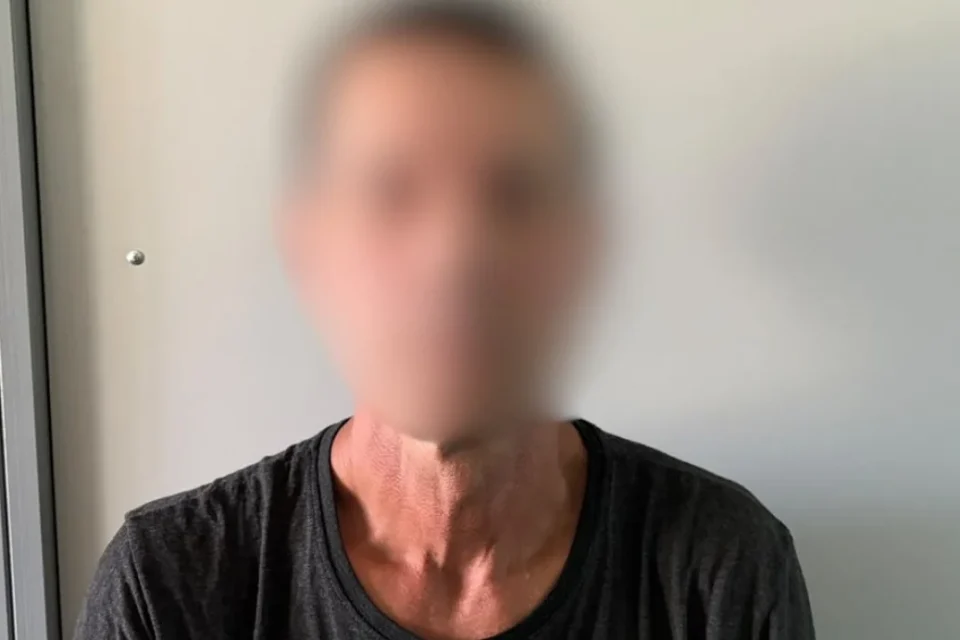 Чоловік у темній футболці з розмитим обличчям біля світлої стіни