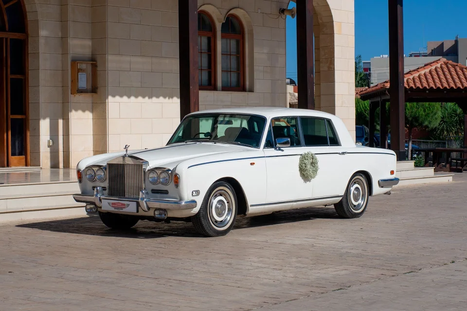 Білий класичний Rolls-Royce біля кам’яної будівлі з арками